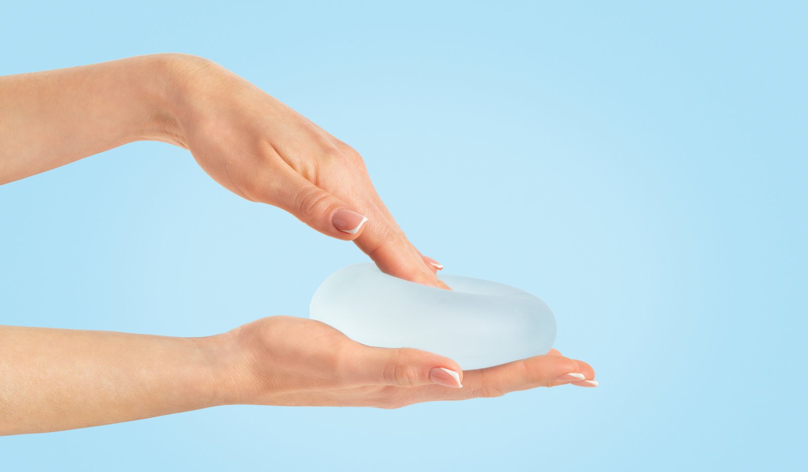 Hand pressing soft breast implant in hand on blue background, copy space.